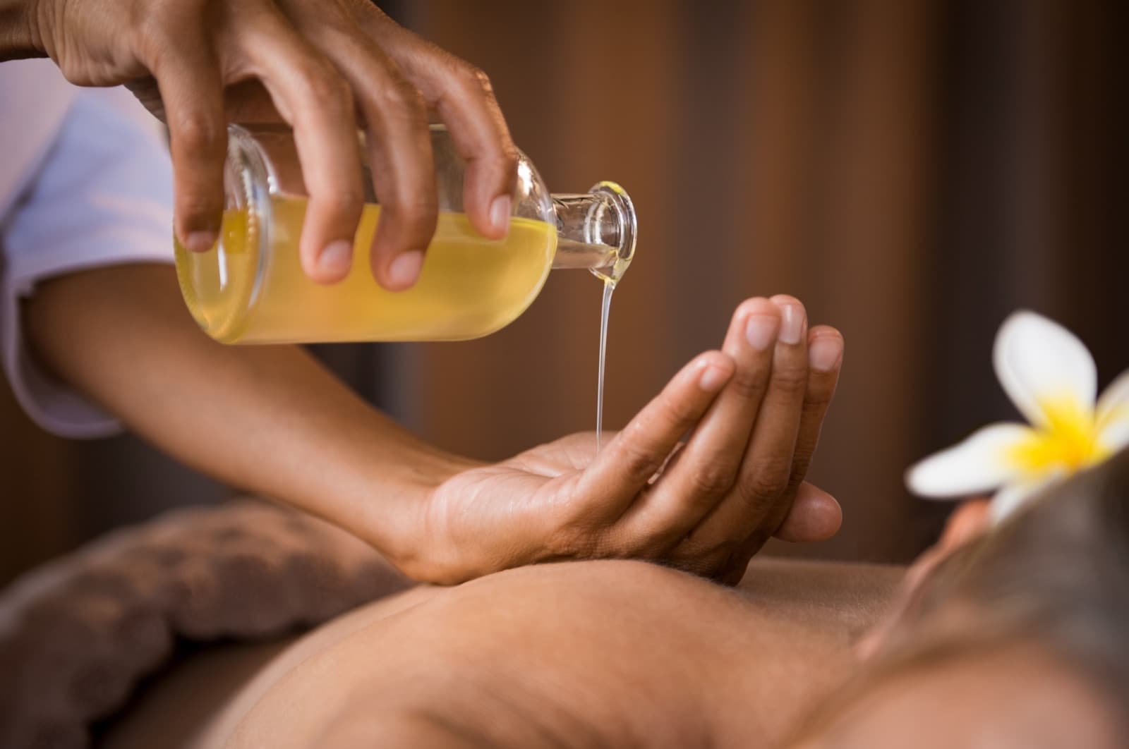 Warm oil being poured into a therapist's hand before a massage