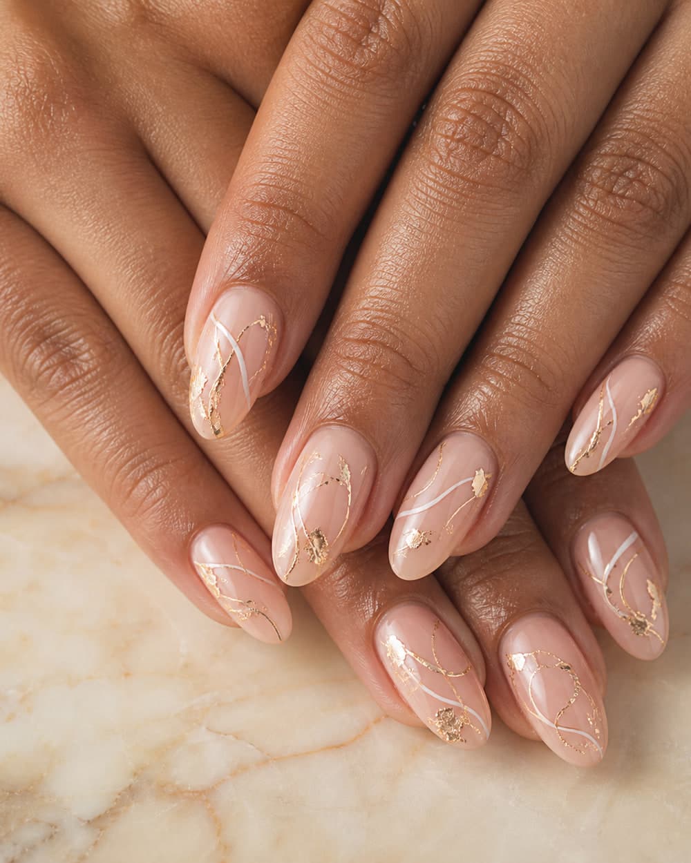 Nude almond nails finished with gold foil and fine white linework