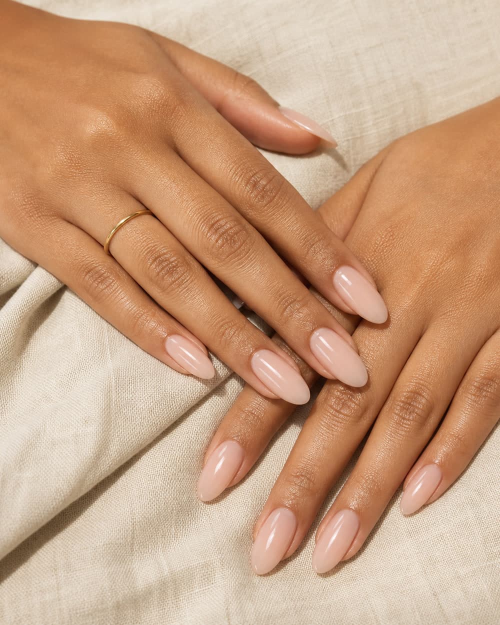 Long nude almond gel nails on two hands resting on cream linen