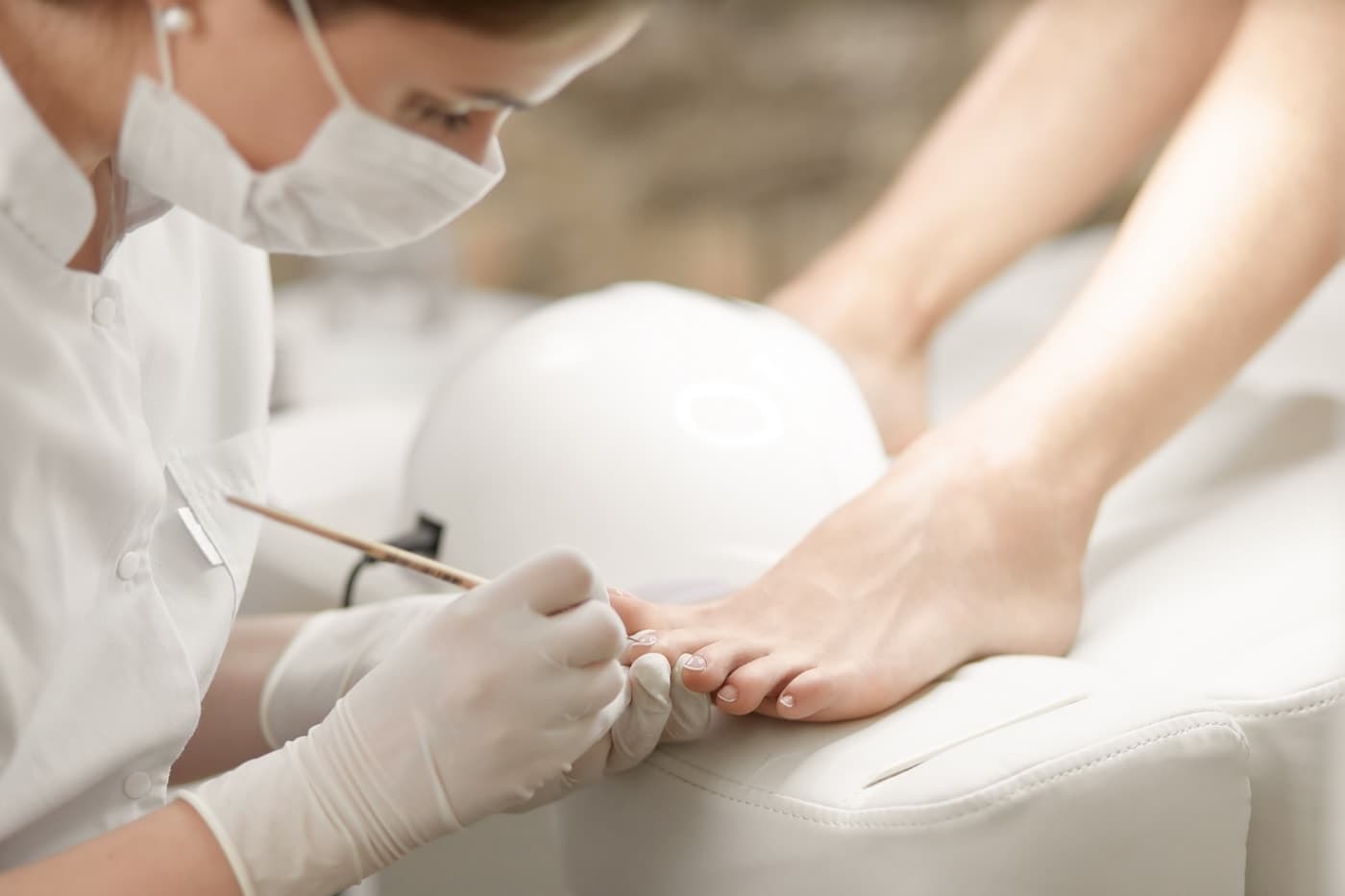Polish being applied to toenails under a lamp during a pedicure