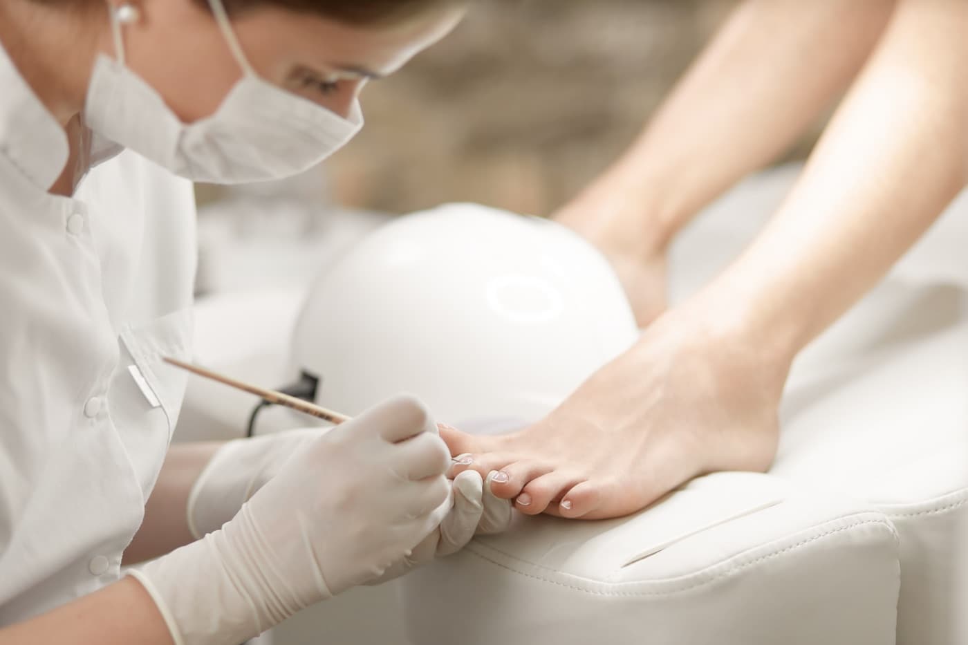 Polish being applied to toenails under a lamp during a pedicure